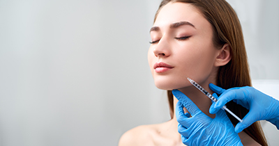 Smile lifting and lip augmentation. Beautician doctor hands doing beauty procedure to female face with syringe. Young woman's mouth countouring with filler injection. Marionette lines treatment